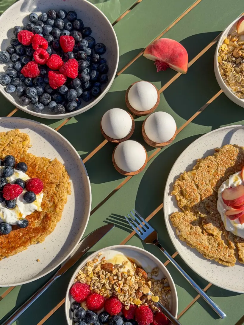 Ontbijt buiten aan tafel met bessen, eitjes, granola en pannenkoekjes