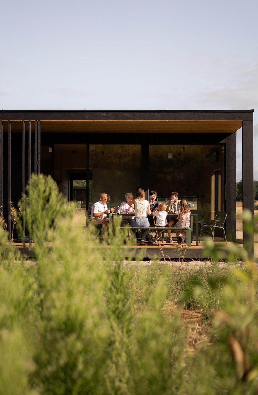 Eco Lodge De Adem: zwarte houten lodge met een glazen pui over de volle breedte, aan de rand van een dennenbos